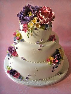 a three tiered white cake with flowers on it's sides and pearls around the edges