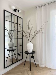 a white vase sitting on top of a wooden table next to a mirror and side table