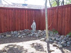 there is a statue in the yard next to a tree and fence with rocks on it