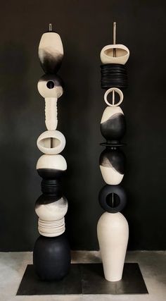 three black and white vases sitting on top of each other in front of a gray wall