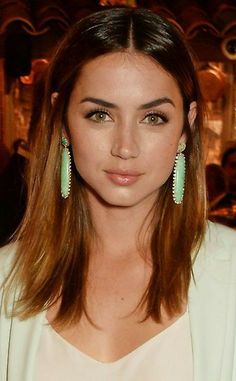 a woman with long hair wearing green earrings and a white blazer is looking at the camera