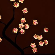 a lighted tree with pink and yellow flowers on it's branches in front of a dark background