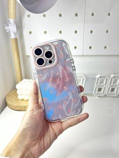 a hand holding an iphone case with blue and pink designs on it, in front of a white wall