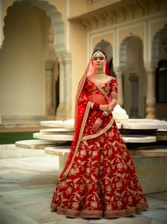 a woman in a red and gold bridal gown standing on a stone floor with her hands on her hips