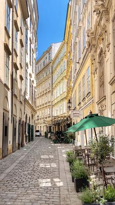 an empty cobblestone street with tables and umbrellas in the middle of it