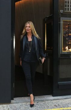 a woman walking out of a building with her hand in her pocket and wearing black