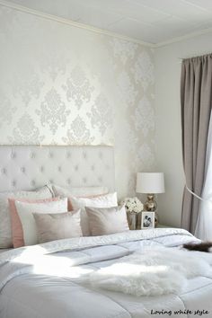 a white bed sitting in a bedroom next to a window with drapes on it