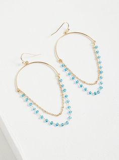 a pair of gold hoop earrings with blue beads and chains on top of white surface