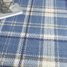 a blue and yellow plaid rug on the floor next to a vase with a candle