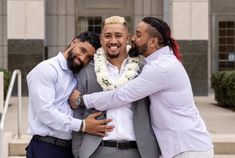 three men hugging each other in front of a building