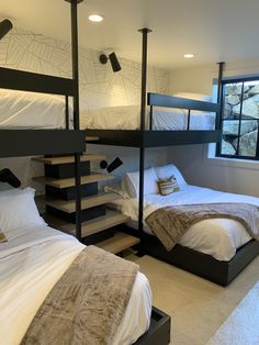 bunk beds in a room with white sheets and pillows on the bottom floor, next to a window
