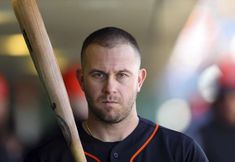 a close up of a baseball player holding a bat and wearing a black shirt with an orange trim