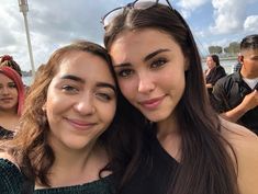 two young women taking a selfie in front of a group of people at an outdoor event