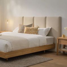 a bed with white sheets and pillows on top of it next to a wooden night stand