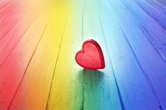 a red heart sitting on top of a rainbow colored wooden floor