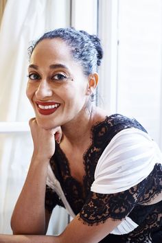 a smiling woman sitting at a table with her hand on her chin and looking off to the side