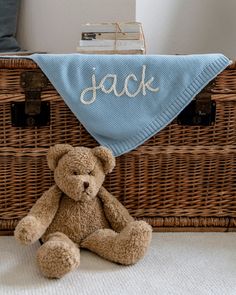 a teddy bear sitting in front of a basket with a blanket on it's back