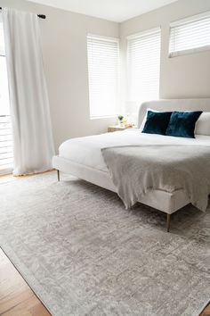 a white bed sitting on top of a wooden floor in a bedroom next to two windows