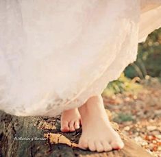 a woman in white dress standing on top of a tree stump with her bare feet