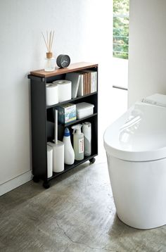 a white toilet sitting next to a wooden shelf filled with bottles and other bathroom items