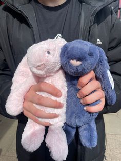 the man is holding two stuffed animals in his hands, one blue and one pink