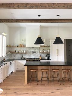 a large kitchen with white cabinets and black counter tops, two pendant lights hanging over the island