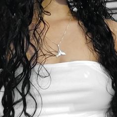 a woman with long black hair wearing a white top and silver necklace on her neck