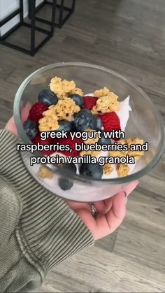 a person holding a glass bowl filled with cereal yogurt and raspberries