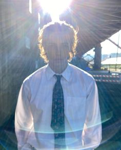 a man wearing a white shirt and tie standing in front of a building with the sun shining on him