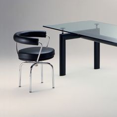 a glass table with a black chair next to it on a white floor and gray background