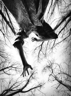 black and white photograph of person reaching up into the sky with trees in the background