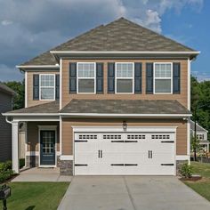 a two story house with brown siding and white garage doors