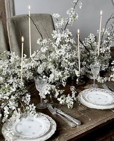 the table is set with white flowers and silverware, candlesticks and plates