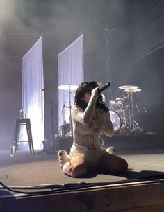 a woman sitting on the floor with her legs crossed and holding a microphone in front of her