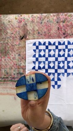 a woman holding up a piece of art with blue and white designs on it's sides