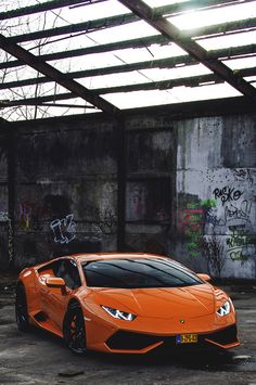 an orange sports car parked in front of a graffiti covered building with windows on the roof
