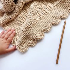 a child's hand is on the edge of a crocheted blanket next to a pencil