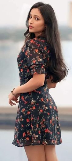 a woman with long dark hair wearing a black floral dress and holding her hand on her hip