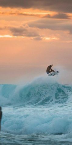 a man riding a surfboard on top of a wave in the ocean at sunset