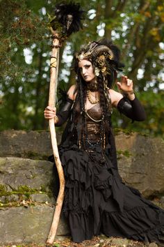 a woman dressed in black sitting on the ground holding a stick and wearing an elaborate headdress