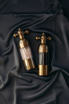 two gold and black bottles sitting next to each other on a dark cloth covered surface