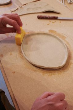 two hands are using a sponge to clean a plate on a table with utensils