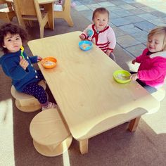 three children sitting at a wooden table eating