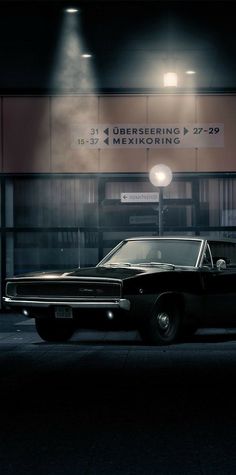 an old black car parked in front of a building at night with the lights on