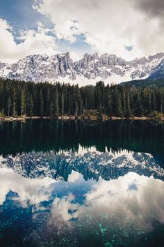 the mountains are reflected in the still water on the lake's surface as clouds hover over them