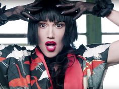 a woman with black hair and red lipstick holding her hands up to her head in front of her face