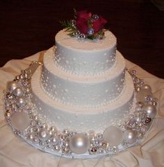 a three tiered wedding cake with pearls and a rose on top is sitting on a white tablecloth