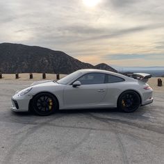 a silver sports car parked on top of a parking lot next to a mountain range