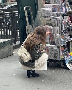 a woman squatting down next to a pile of newspapers on the side of the street