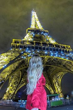 a woman standing in front of the eiffel tower at night with her back to the camera